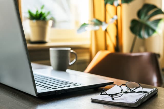 A sunlit workspace with a laptop, notebook and coffee